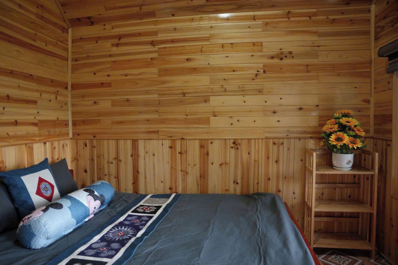 Una habitación con paneles de madera, una cama, almohadas, un colcha y un estante con un arreglo floral.