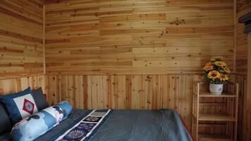 Una habitación con paneles de madera, una cama, almohadas, un colcha y un estante con un arreglo floral.