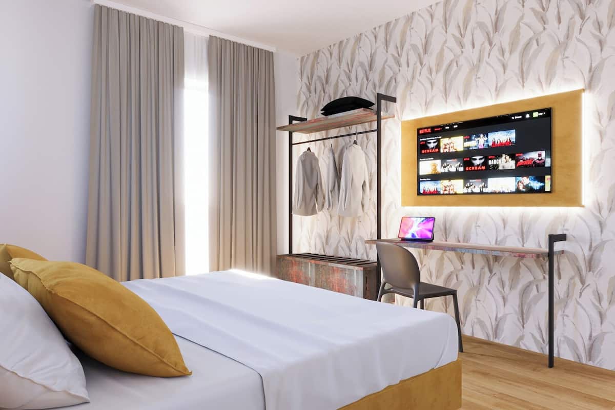 Ein modernes Hotelzimmer mit Bett, Schreibtisch und einem an der Wand befestigten Fernseher, der eine Netflix-Oberfläche zeigt.