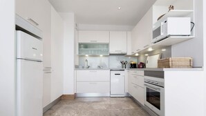 Una cocina moderna con armarios blancos, microondas integrado, lavavajillas y horno.