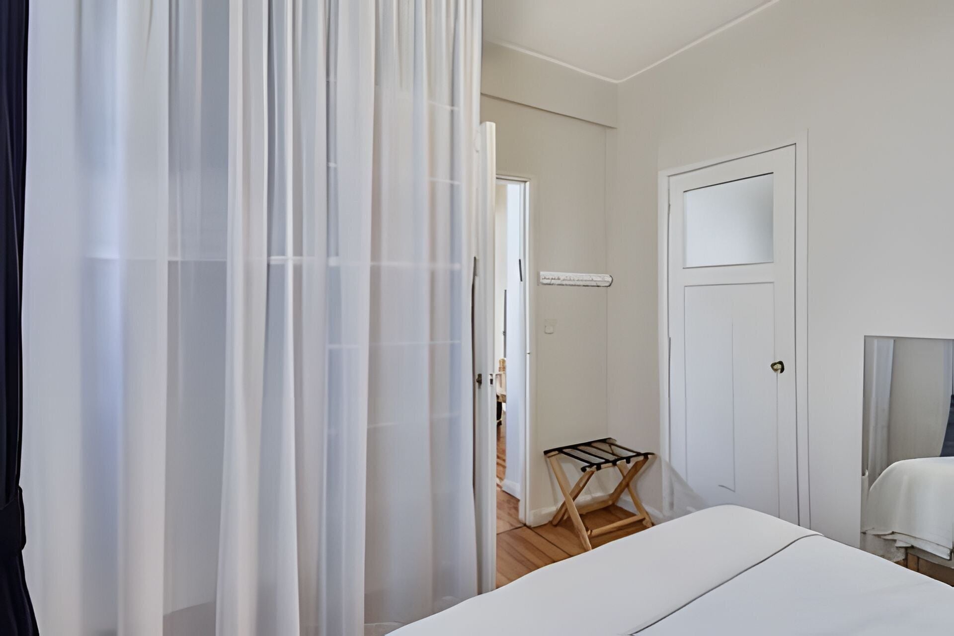 Een slaapkamer met een bed, een deur, een raam en een houten vloer.