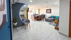 Een moderne woonkamer met een eethoek, een bank en een aan de muur bevestigde televisie.
