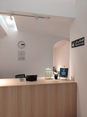 A reception desk with a clock, a sign indicating the reception area, and a digital display board. - Five Hours (Buraydah)