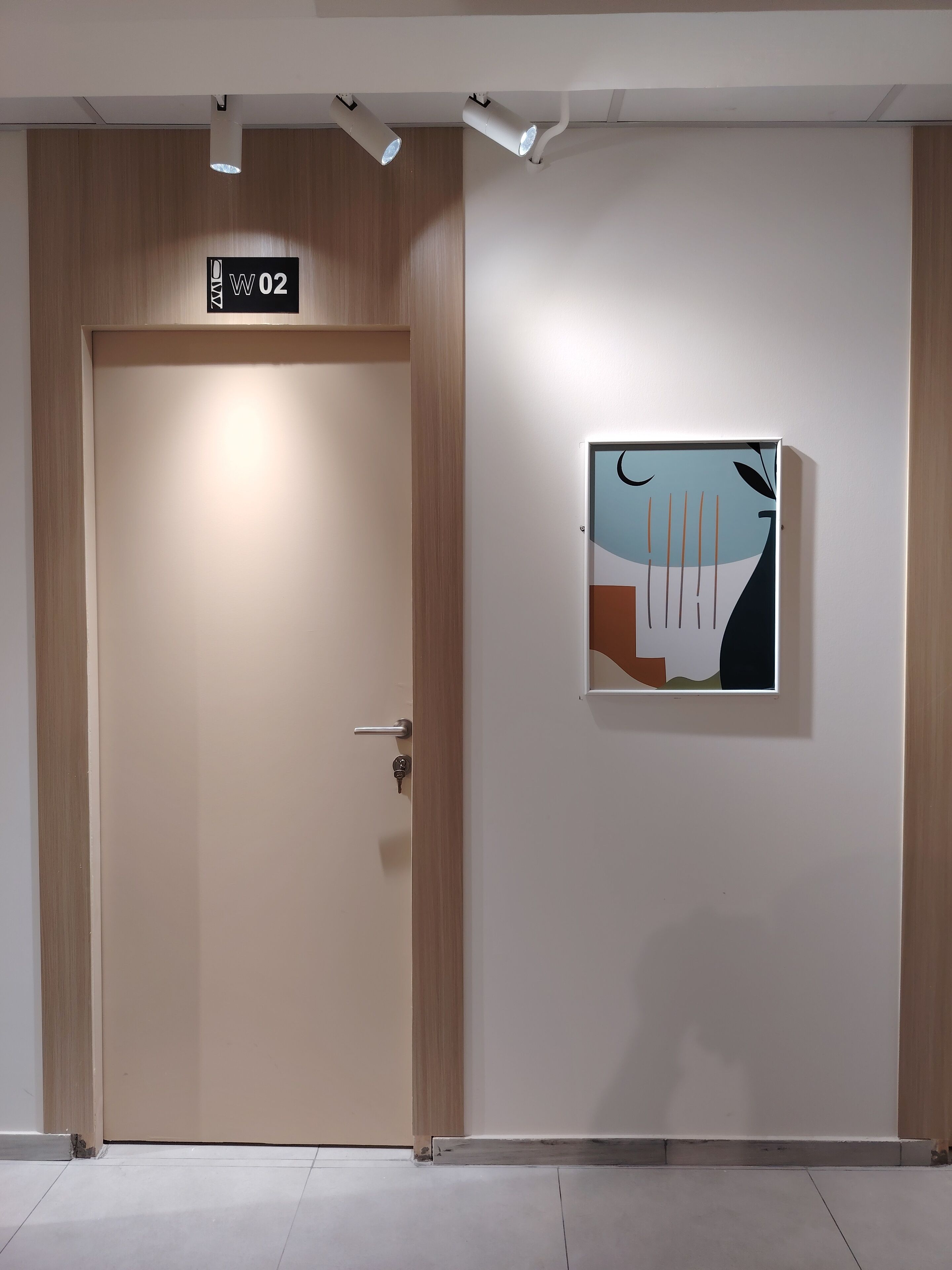 A hotel room entrance with a door marked "W02", a light fixture above, and a wall-mounted abstract art piece.