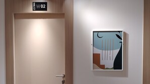 Entrada a una habitación de hotel con una puerta marcada "W02", una lámpara encima y una obra de arte abstracto colgada en la pared.