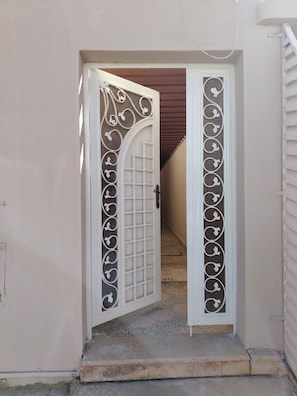 A white door with decorative patterns and a grid design, leading to a hallway. - Five Hours (Buraydah)