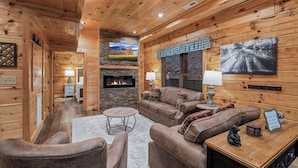 A cozy log cabin interior with a fireplace, comfortable seating, and a television. - Tennessee Time is always right (PIGEON FORGE)
