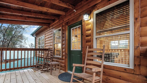 A log cabin with a wooden deck, a green door, and a rocking chair. - Tennessee Time is always right (PIGEON FORGE)