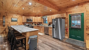 A wooden cabin-style kitchen with a central island, stainless steel appliances, and a green door. - Tennessee Time is always right (PIGEON FORGE)