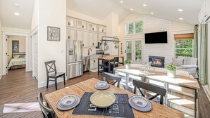 A modern kitchen with white cabinets, a dining area with a wooden table, and a living space with a fireplace. - Red Roof Retreat at Lake Anna, Waterfront w/kayaks, fire pit, grill & large deck (Bumpass)