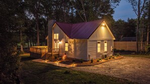 A small, single-story cabin with a wooden deck and a red roof, surrounded by trees. - Red Roof Retreat at Lake Anna, Waterfront w/kayaks, fire pit, grill & large deck (Bumpass)