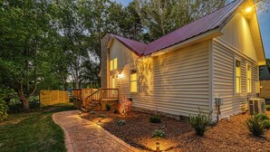 A two-story house with a stone pathway leading to the front door, surrounded by a well-maintained garden and a wooden fence. - Red Roof Retreat at Lake Anna, Waterfront w/kayaks, fire pit, grill & large deck (Bumpass)