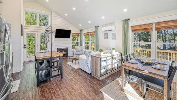 A spacious kitchen with a dining area, a fireplace, and a large window overlooking a deck. - Red Roof Retreat at Lake Anna, Waterfront w/kayaks, fire pit, grill & large deck (Bumpass)