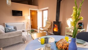 Una sala de estar acogedora con un sofá, una mesa de comedor dispuesta para el desayuno, un televisor y una chimenea.