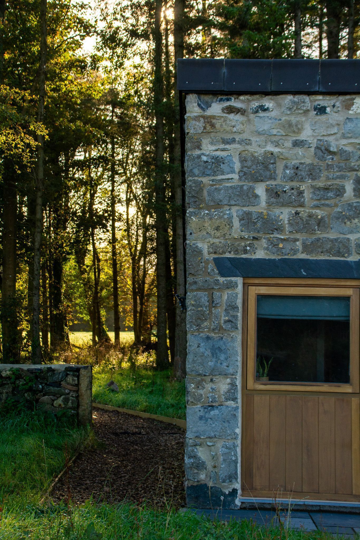 Ein Steingebäude mit einer Holztür und einem Fenster, umgeben von einem Wald.