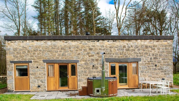 Un edificio de piedra con dos puertas de madera, un jacuzzi y un patio con una mesa y sillas.