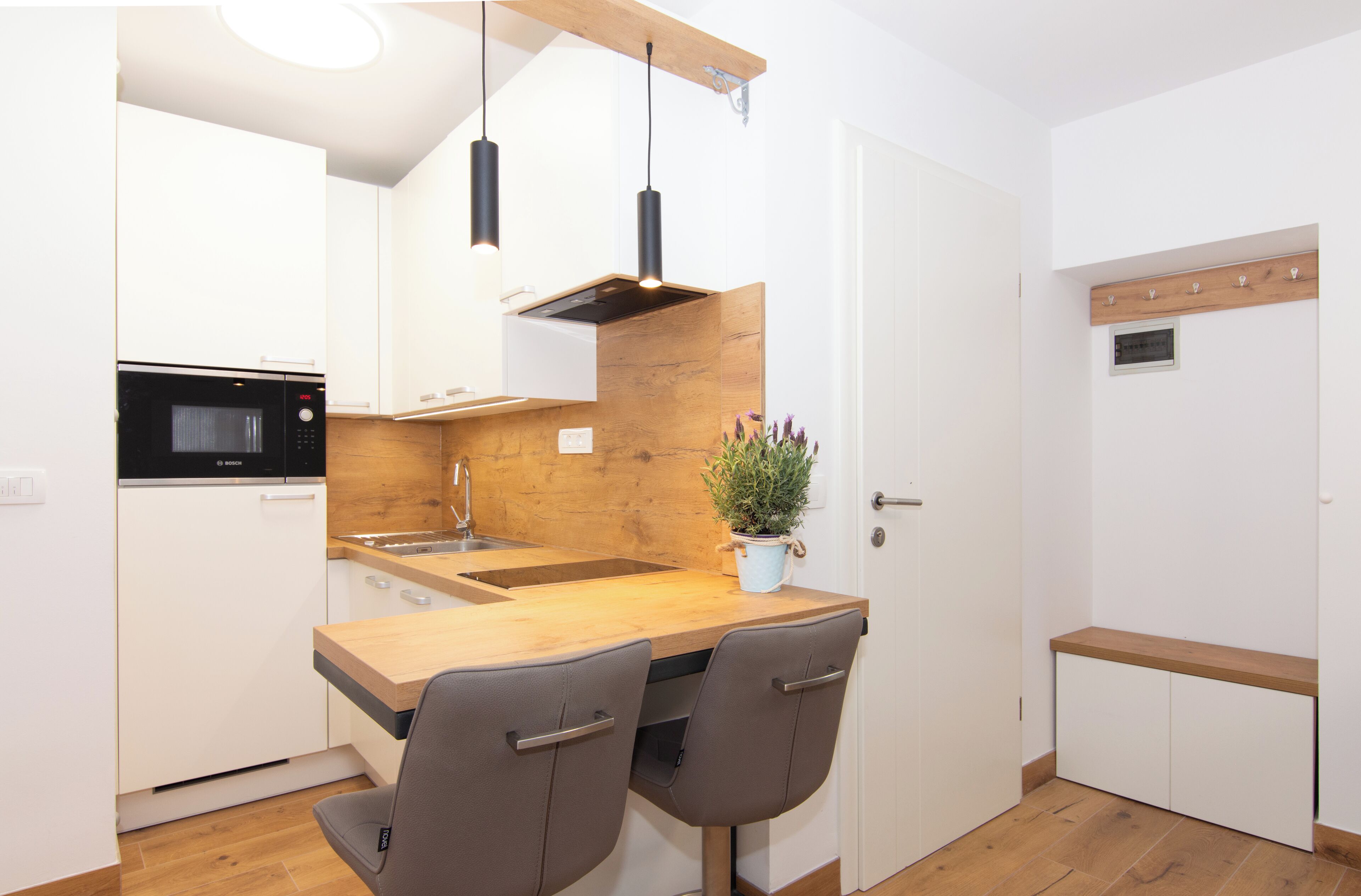 A compact kitchen with white cabinets, a wooden countertop, a Bosch microwave, and two chairs.