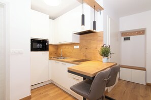 Une cuisine compacte avec des meubles blancs, un plan de travail en bois, un four encastré et des luminaires suspendus.