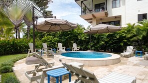 A pool area with lounge chairs, umbrellas, and a building in the background. - Elegant 3 BR Ground-Floor Apartment with Hot Tub (Cocle)