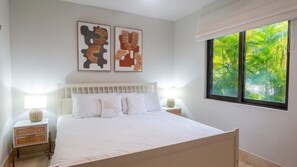 A bedroom with a bed, two bedside tables, a window with a view of greenery, and two wall-mounted artworks. - Elegant 3 BR Ground-Floor Apartment with Hot Tub (Cocle)