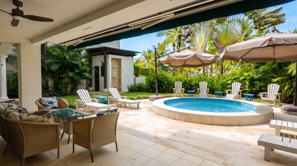 A pool area with lounge chairs, a hot tub, and umbrellas.