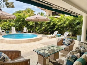 A pool area with lounge chairs and umbrellas, surrounded by lush greenery.
