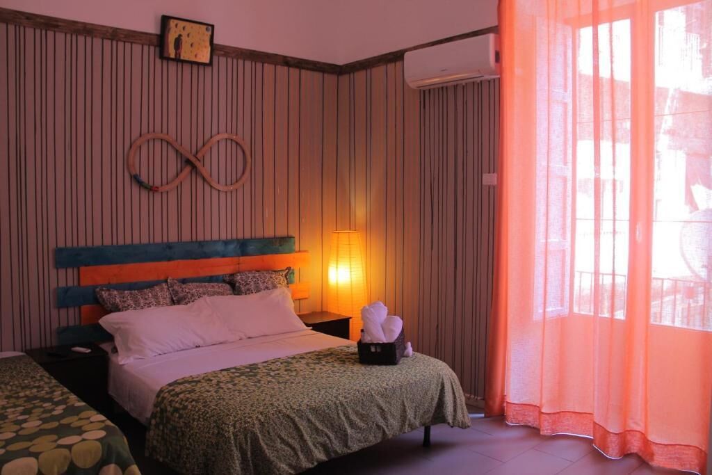 Une chambre d’hôtel avec un lit, une table de chevet, une horloge murale et une fenêtre avec des rideaux.