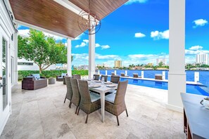 An outdoor patio with a dining table and chairs, overlooking a swimming pool and city skyline. - Waterfront Gem! Heated Pool+HotTub! Close 2 Beach! (Pompano Beach)