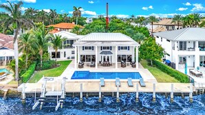 A large house with a swimming pool, surrounded by palm trees and a view of the water. - Waterfront Gem! Heated Pool+HotTub! Close 2 Beach! (Pompano Beach)