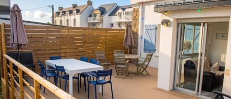 A wooden deck with a table and chairs, a glass door entrance, and a wooden fence.