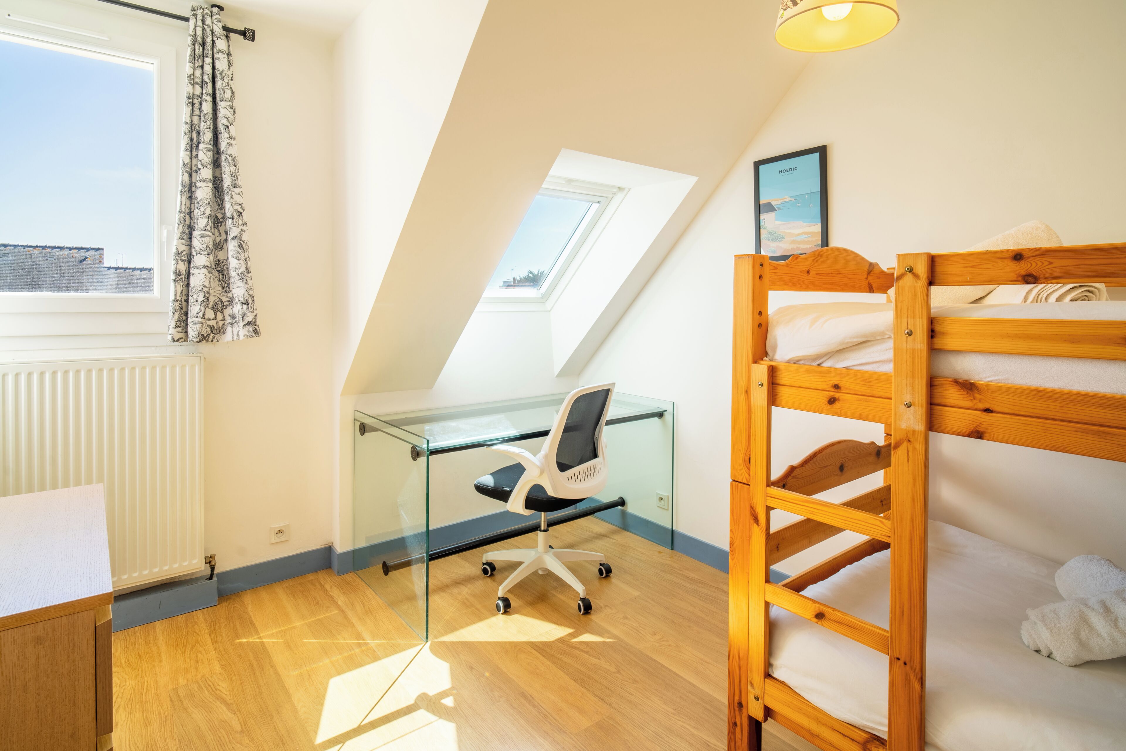 Une chambre de dortoir avec un lit superposé, un bureau avec une chaise, un radiateur, une fenêtre avec des rideaux et un puits de lumière.