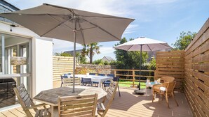 An outdoor deck with wooden furniture, including tables and chairs, and two large umbrellas providing shade. - 3 *** village house, bright veranda opening onto terrace and large garden (Quiberon)