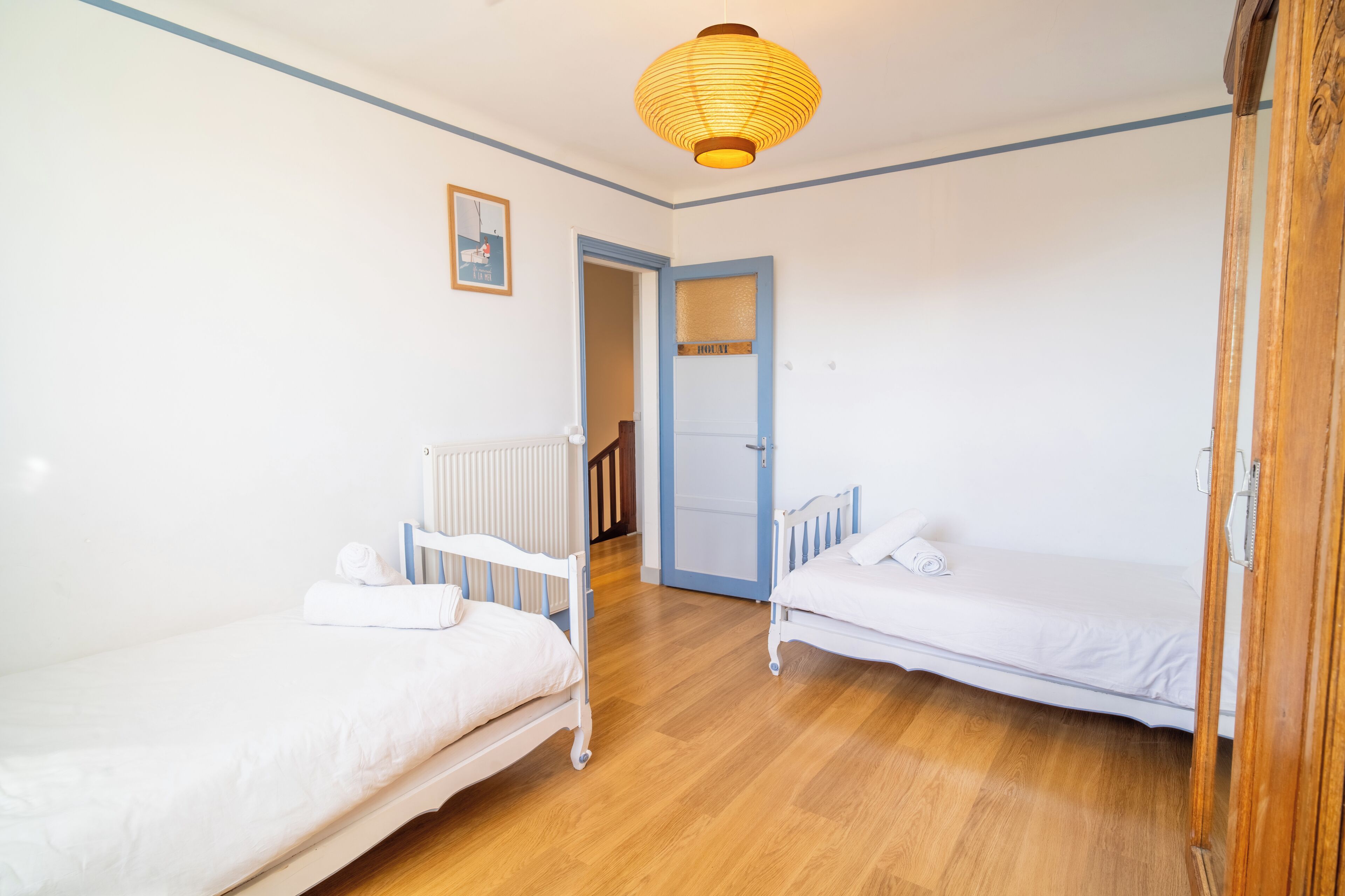 Une chambre avec deux lits simples, un plancher en bois, un radiateur, une porte et un luminaire suspendu.