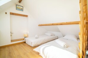 A bedroom with two beds, wooden beams, a door, and a small bedside table with a lamp. - 3 *** village house, bright veranda opening onto terrace and large garden (Quiberon)