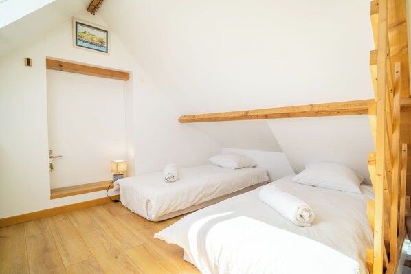 Een slaapkamer met twee bedden, houten balken, een deur en een klein nachtkastje met een lamp.