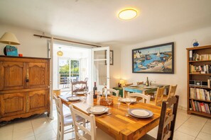 Un comedor con una mesa de madera dispuesta para cuatro, sillas, una estantería y un cuadro en la pared.