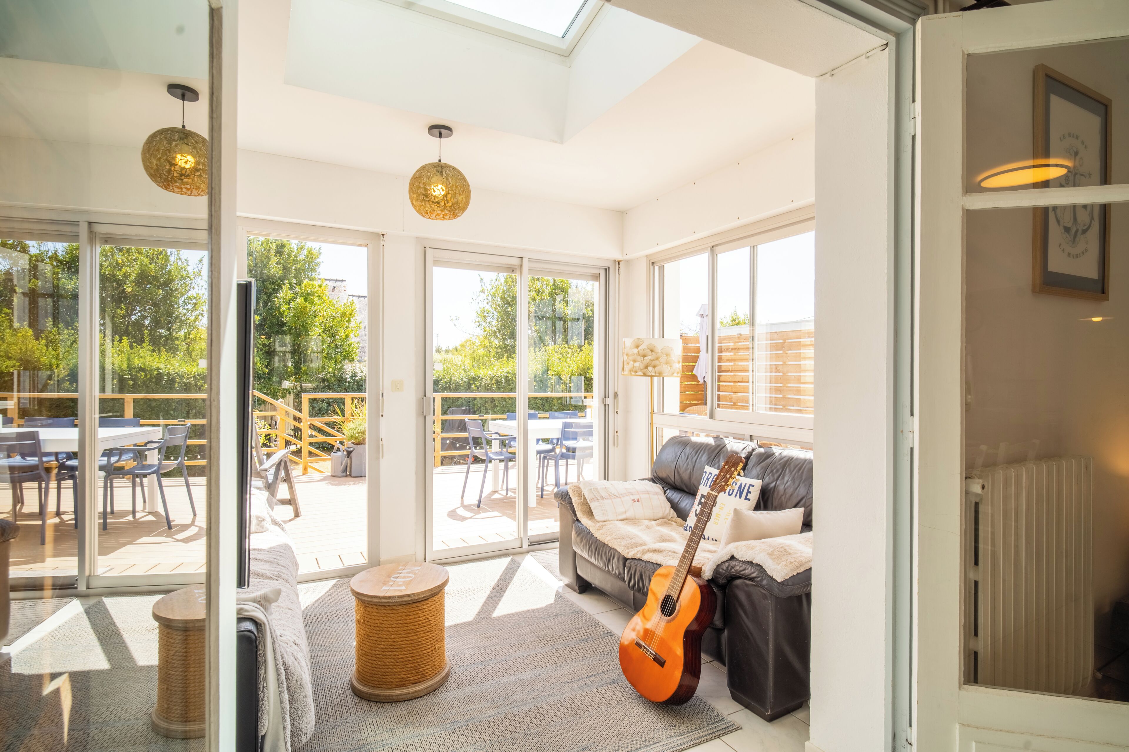A bright room with a large sliding glass door leading to an outdoor deck, a sofa with a guitar, and a woven basket.