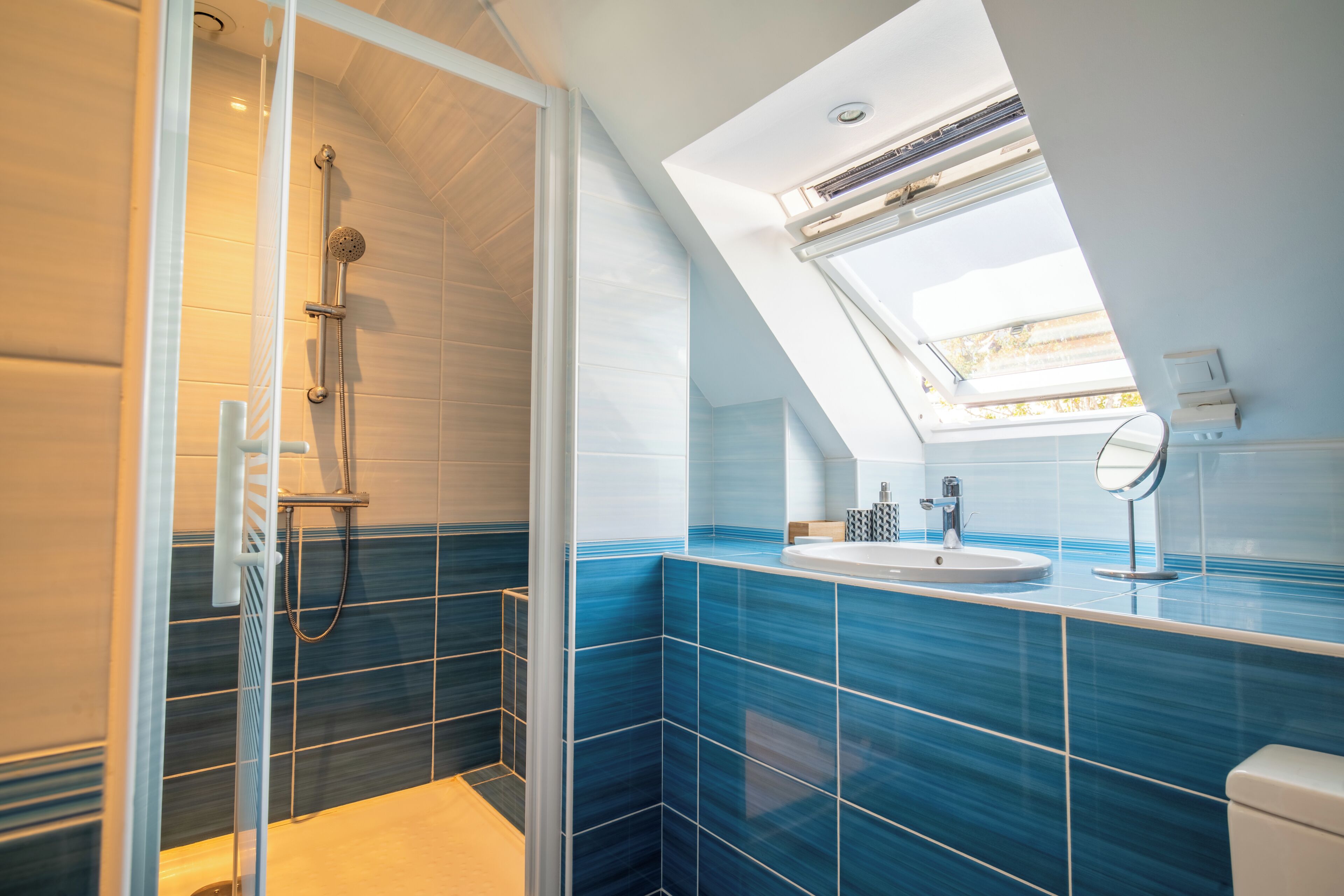 Une salle de bain moderne dotée d’une lucarne, d’une douche et d’un lavabo avec un miroir.