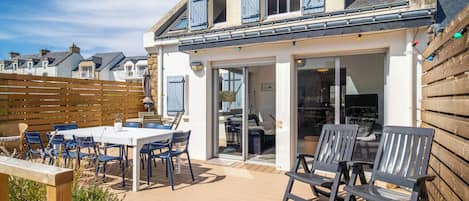 A house with a patio area featuring a table and chairs, a wooden deck, and a view of neighboring houses.