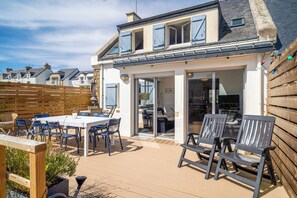 A house with a patio area featuring a table and chairs, a wooden deck, and a view of neighboring houses.