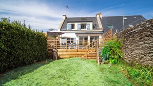 A two-story house with a stone wall, a wooden deck, and a grassy yard. - 3 *** village house, bright veranda opening onto terrace and large garden (Quiberon)