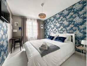 Cozy retreat with a large bed, desk, and potted plant, set against a floral wallpaper backdrop.