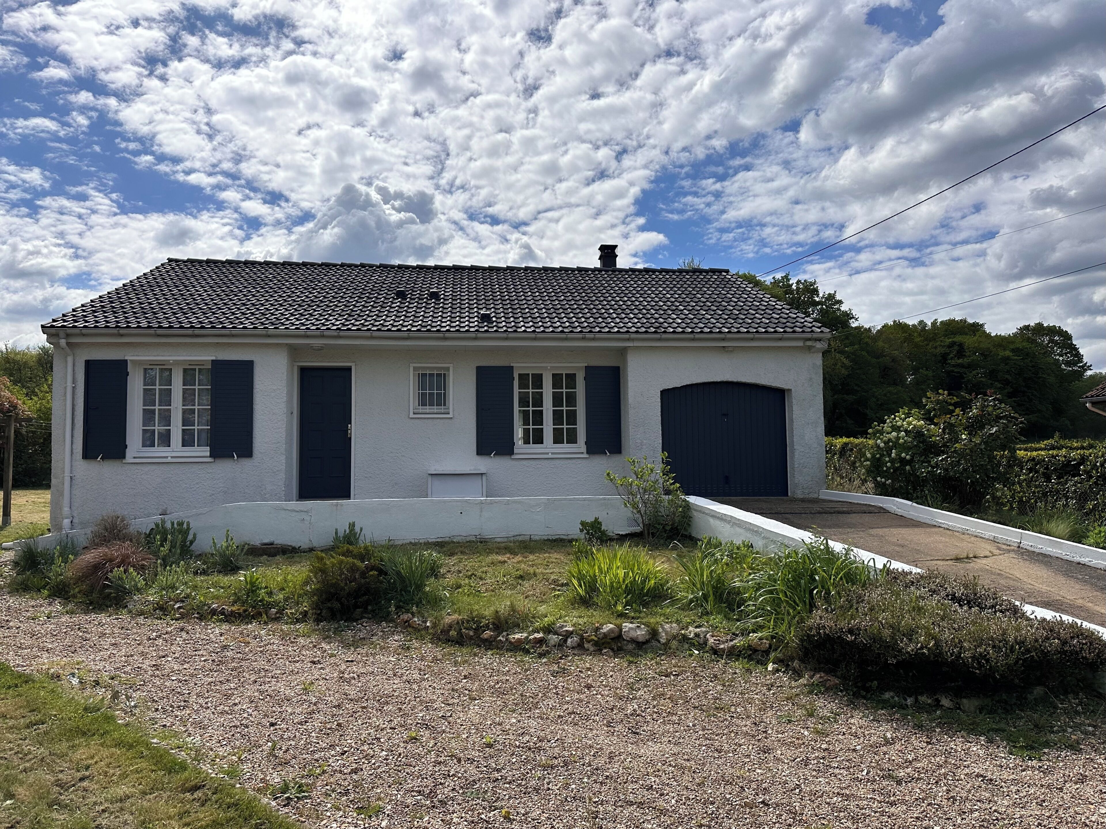 Ein zweistöckiges Haus mit einem Ziegeldach, einer Garage und einer Auffahrt mit Kies.