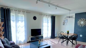 A modern living room with a sofa, coffee table, TV, dining area with chairs, and a decorative wall piece. - Charming Datcha in Normandy  (Les Damps)