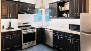 A modern kitchen with dark cabinetry, stainless steel appliances, and a pendant light.