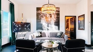 A modern living room with a grey sofa, black chairs, a round coffee table, and a large chandelier.