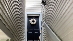 A wooden staircase leading to a dark blue door with a wreath, flanked by white siding walls and a skylight above.