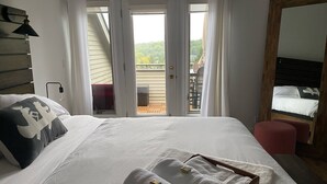 A bedroom with a large bed, a wooden headboard, a nightstand, a mirror, and a view of a balcony with outdoor furniture.