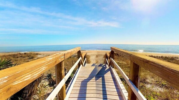A wooden boardwalk leading to a beach with a clear sky.