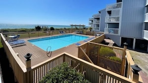 A pool area with a wooden deck, lounge chairs, and a view of the ocean. - Sea Colony B7-one bedroom one bath, 1st floor, oceanfront rental located in Carolina Beach with panoramic views (Carolina Beach)